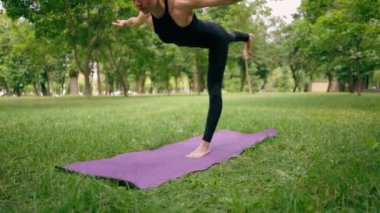 Tecrübeli bir kadın eğitmen parkta meditasyon yapıyor yoga yapıyor tek bacağı esnetiyor ve farklı kas grupları çalıştırıyor.
