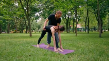 Erkek yoga hocası, parkta bir kadınla birlikte, temiz hava ile ilgili bir ders veriyor. Çift, manevi egzersizler yapıyor.