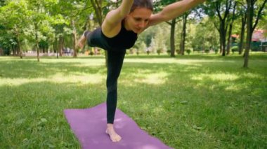 Tecrübeli bir kadın eğitmen parkta meditasyon yapıyor yoga yapıyor tek bacağı esnetiyor ve farklı kas grupları çalıştırıyor.