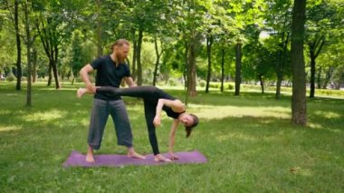 Erkek yoga hocası, parkta bir kadınla birlikte, temiz hava ile ilgili bir ders veriyor. Çift, manevi egzersizler yapıyor.