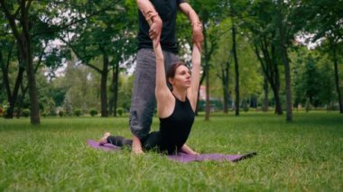 Erkek yoga hocası, parkta bir kadınla birlikte, temiz hava ile ilgili bir ders veriyor. Çift, manevi egzersizler yapıyor.