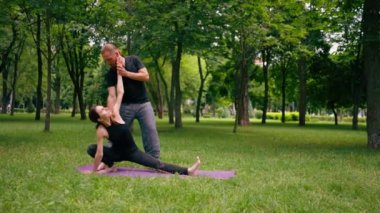 Erkek yoga hocası, parkta bir kadınla birlikte, temiz hava ile ilgili bir ders veriyor. Çift, manevi egzersizler yapıyor.