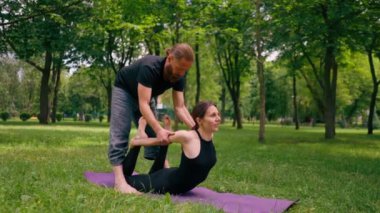 Erkek yoga hocası, parkta bir kadınla birlikte, temiz hava ile ilgili bir ders veriyor. Çift, manevi egzersizler yapıyor.