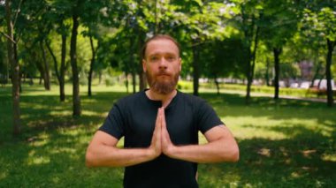 Yakışıklı sakallı adam parkta meditasyon yapıyor. Lotus pozisyonunda oturuyor. Yoga yapıyor.