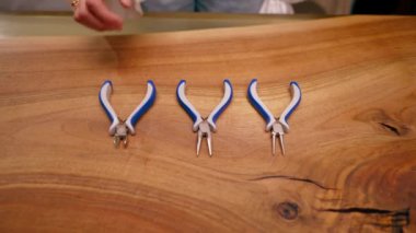 Çalışan aletlerin üst görüntüsü. İğneci kadın el işi mücevherlere başlamadan önce penseyi masaya koyar.