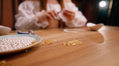 Kendi elleriyle mücevher yapan genç bir kızın elleri pense yapımında kullanılan kolye için tel kalıntılarını kesiyor.