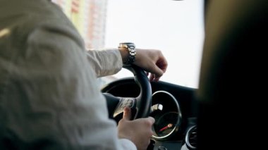 Şehrin içinde lüks bir arabanın içinde direksiyonun başında bir erkek sürücünün saatiyle el ele tutuşun.