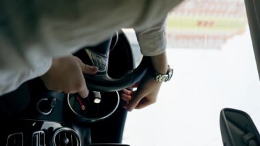 Şehirde lüks bir arabanın içinde direksiyonun başında bir erkek sürücünün kol saatiyle el ele çekilmiş dikey video görüntüsü.