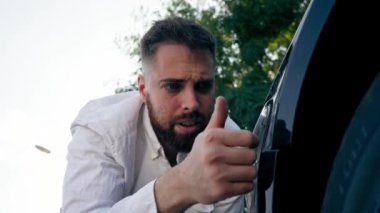 Yakın plan üzgün sakallı adam kaza üstüne çarpışan siyah arabayı kontrol ediyor.