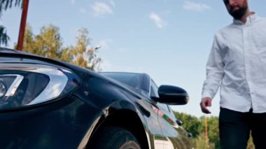 Yakın plan üzgün sakallı adam kaza üstüne çarpışan siyah arabayı kontrol ediyor.