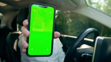 Yakın plan gülümseyen sakallı iş adamı. Lüks araba kullanırken yeşil ekranlı telefonu gösteriyor.