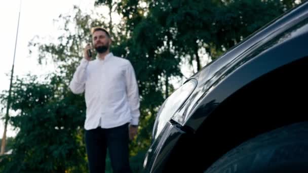 Ένας Γενειοφόρος Άνδρας Στέκεται Κοντά Ένα Μαύρο Πολυτελές Αυτοκίνητο Μιλάει — Αρχείο Βίντεο