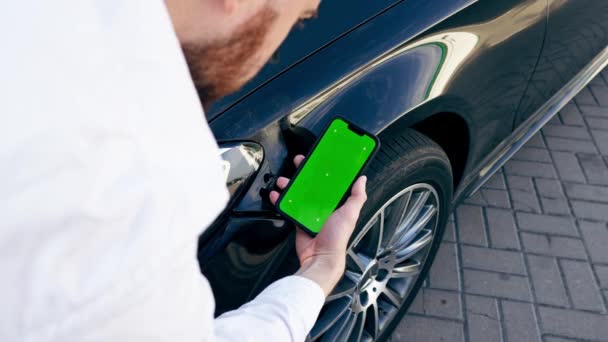 彼の手の緑の画面でスマートフォンで旅行中に事故の後 黒い車の損傷したバンパーをチェックする男性のクローズアップ — ストック動画