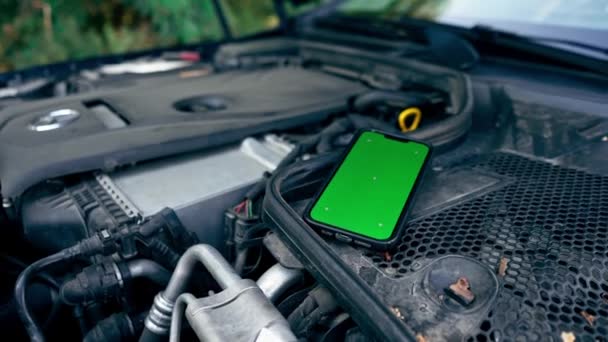 在检查油电池电平的同时 将装有绿色屏幕的智能手机的特写放在汽车引擎上 — 图库视频影像