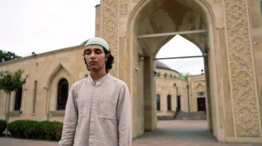 Müslüman bir caminin arka planında kameraya bakan genç bir Arap 'ın portresi