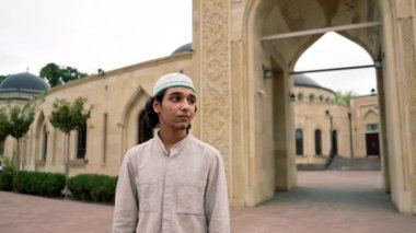 Müslüman bir caminin arka planında kameraya bakan genç bir Arap 'ın portresi