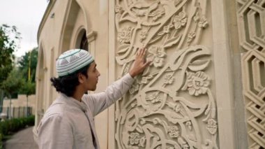 Müslüman bir adam cami girişindeki kemerdeki İslami süsü hevesle inceliyor.
