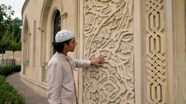 Müslüman bir adam cami girişindeki kemerdeki İslami süsü hevesle inceliyor.