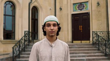 Müslüman bir caminin arka planında kameraya bakan genç bir Arap 'ın portresi