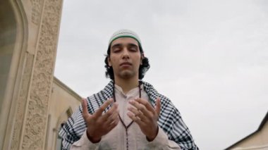Ulusal giysiler içinde, boynunda tespihle cami avlusunda dua eden Arap bir adam.