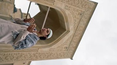 Ulusal giysiler içinde, boynunda tespihle cami avlusunda dua eden Arap bir adam.