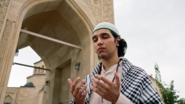 Ulusal giysiler içinde, boynunda tespihle cami avlusunda dua eden Arap bir adam.