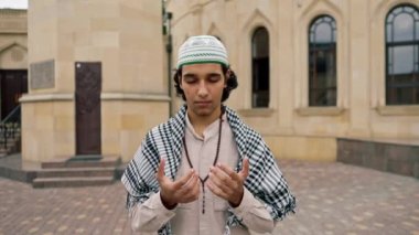 Ulusal giysiler içinde, boynunda tespihle cami avlusunda dua eden Arap bir adam.