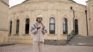 Ulusal giysiler içinde, boynunda tespihle cami avlusunda dua eden Arap bir adam.