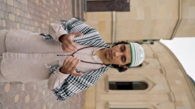 Ulusal giysiler içinde, boynunda tespihle cami avlusunda dua eden Arap bir adam.