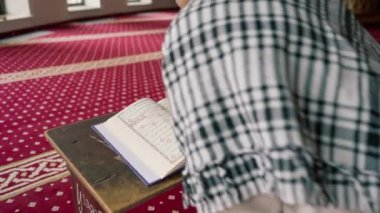 Müslüman bir adam Kuran 'ı dikkatle okur ve camide Allah' a dua eder.