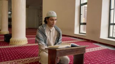 Müslüman bir adam, kutsal mescitteki halıda sessizce oturup Kuran okuyarak Allah 'a yöneldi.