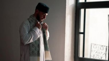 Bir Arap rahibin silueti, ulusal giysiler içinde bir camide duruyor ve Kuran 'ın yardımıyla Ramazan' da Allah 'a dua ediyor.