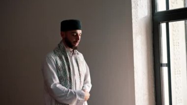 Bir Arap rahibin silueti, ulusal giysiler içinde bir camide duruyor ve Kuran 'ın yardımıyla Ramazan' da Allah 'a dua ediyor.