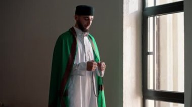 Bir Arap rahibin silueti, ulusal giysiler içinde bir camide duruyor ve Kuran 'ın yardımıyla Ramazan' da Allah 'a dua ediyor.