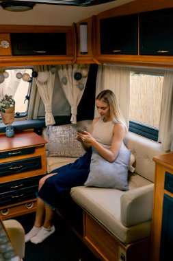 Oturma odasındaki kanepede dinlenen genç bir kız telefona bakıyor ve gülümsüyor.