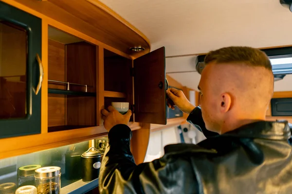 A man opens drawers and cabinets in the kitchen in search of a cup to make tea in a motor home
