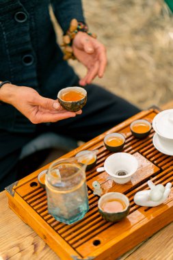 Çaydanlıktan taze yeşil çay dolduran profesyonel bir çay ustasının elleri ahşap bir chaban masasında kaselere doldurur.