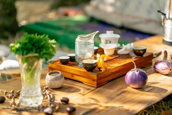 A wooden stand with bowls filled with water and cups of tea stands on the table among greens and vegetables