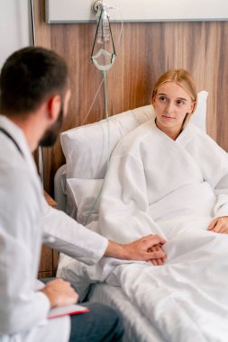 Doktor hasta kıza bir hastane odasında destek oluyor ve iyileşmesi için elini tutuyor.