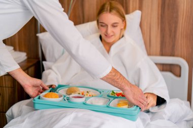 Hastane odasında yatan bir kız, gücünü arttırmak ve hastalıktan kurtulmak için lezzetli bir yemekle birlikte tepsiye konur.