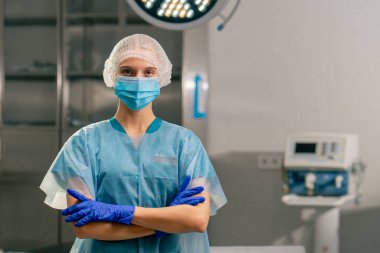 Üniformalı bir kadın anestezi uzmanı portresi ve ameliyat odasında kollarını önünde kavuşturmuş bir tıbbi maske.