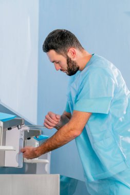 Tıp üniformalı bir doktor ellerini musluğun altında yıkıyor ve işe gitmeden önce antiseptikle dezenfekte ediyor.