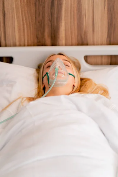 Close-up shot of a girl lying in hospital room wearing an oxygen mask to a maintain breathing during illness