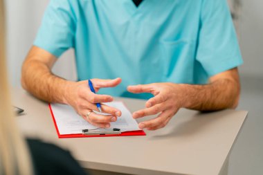 Hastaya aktif olarak el kol hareketi yapan ve hastalığının sebebini açıklayan bir doktorun elleri.