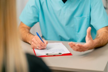 Hastaya aktif olarak el kol hareketi yapan ve hastalığının sebebini açıklayan bir doktorun elleri.