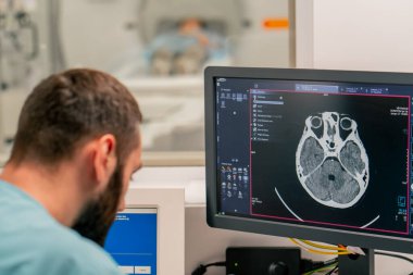 Bir radyolog bilgisayar monitörünün arkasındaki masada oturur ve bir hastanın muayenesi sırasında manyetik rezonans görüntüleme görüntüsünü inceler.