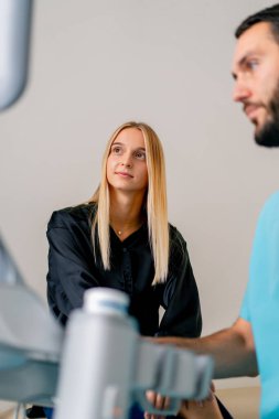 Hasta bir kız, doktoruyla oturur ve ultrason makinesinin monitörüne dikkatlice bakar.