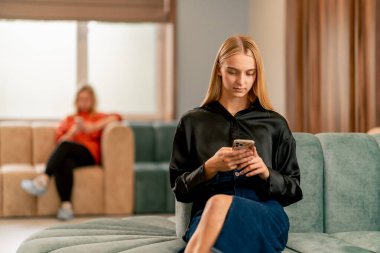 Elinde telefon olan bir kız kliniğin koridorunda oturmuş doktordan randevu bekliyor.