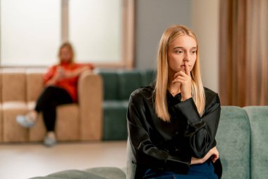 Hastanenin lobisinde oturmuş doktorunu bekleyen üzgün ve düşünceli bir kızın portresi.