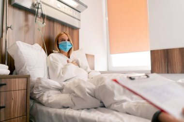 Karantinada, hastane odasında, tıbbi maskeli bir kız, sağlığıyla ilgili bir doktora şikayette bulunuyor.